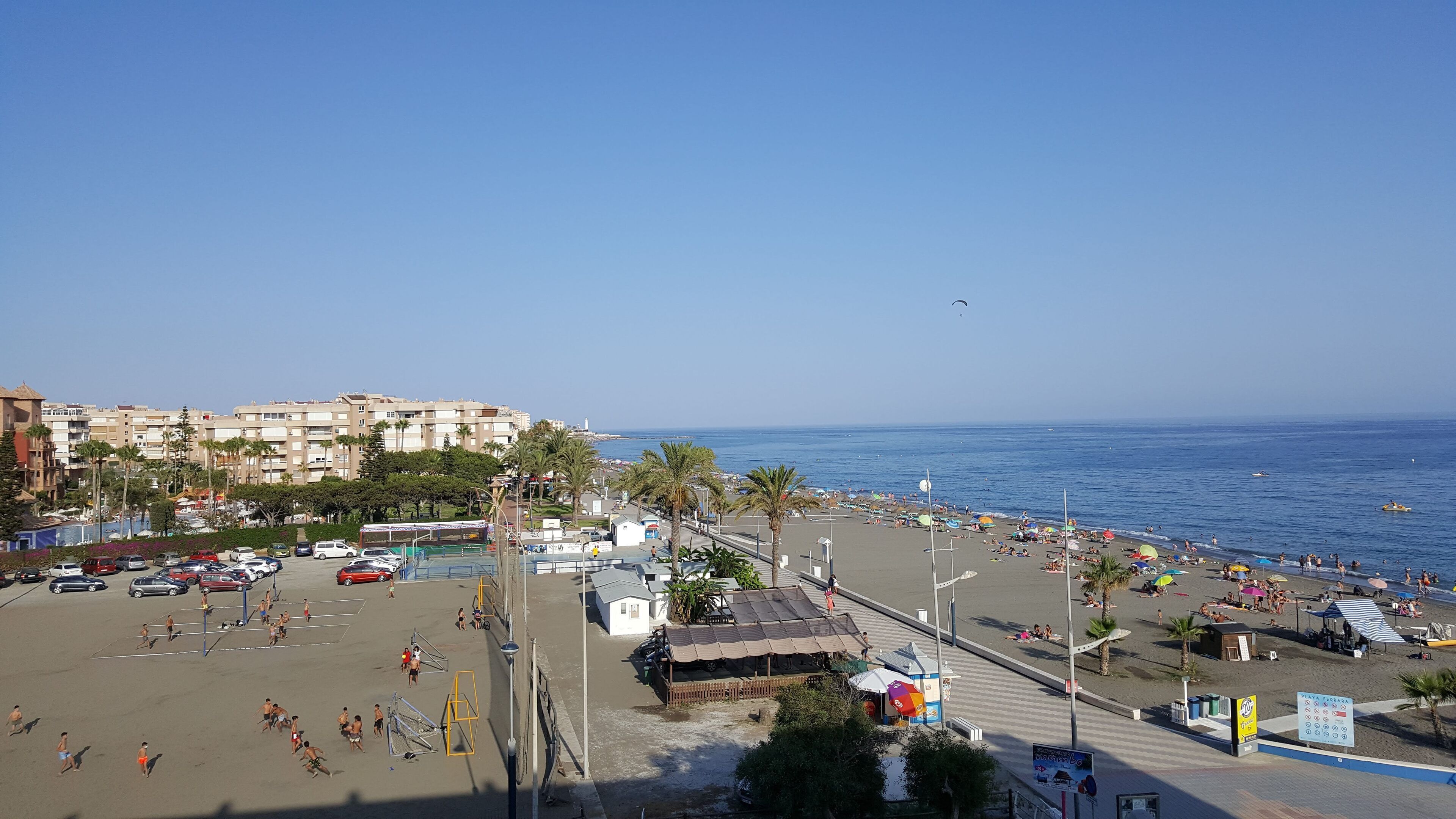A beach with a parking area, a small kiosk, and a view of the sea.