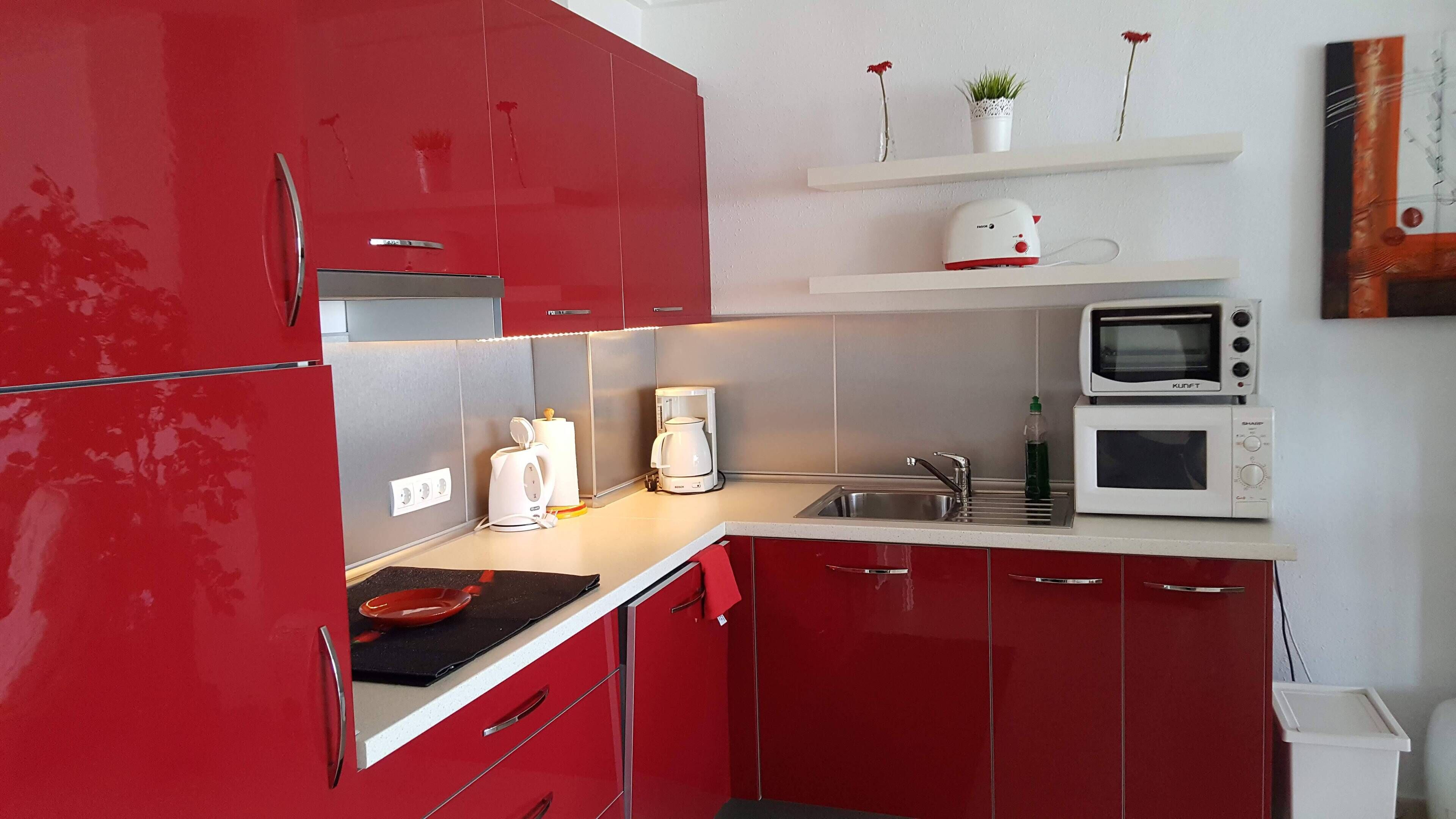 Una cocina compacta con armarios rojos, una cafetera, un microondas y un estante pequeño con adornos.