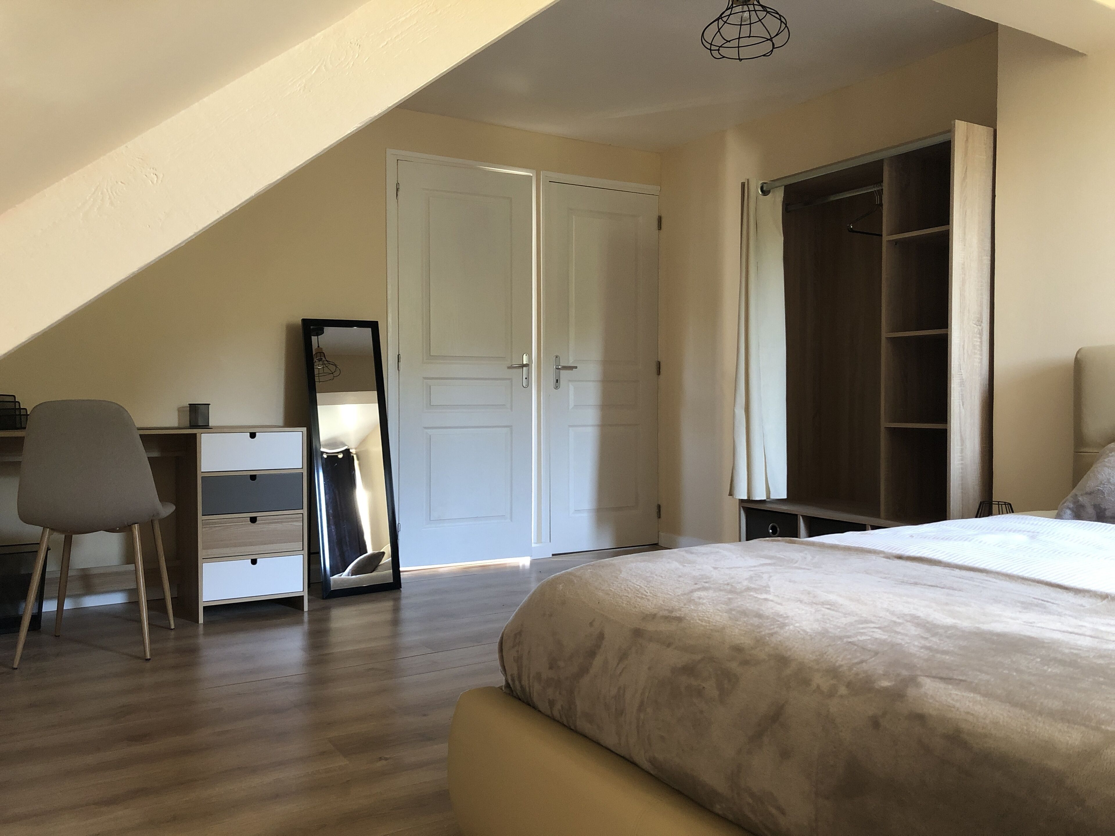 Une chambre à coucher comprenant un lit, un bureau, une chaise, une armoire et un miroir.