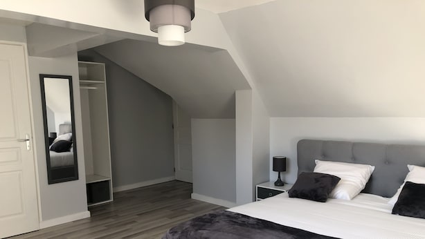Een moderne slaapkamer met een groot bed, een nachtkastje, een spiegel en een garderobe.