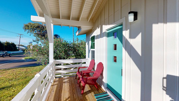 Una terraza de madera con sillas Adirondack rojas, una barandilla de porche blanca y una puerta turquesa.