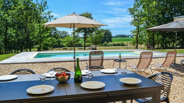 Ein Essbereich im Freien mit Pool, umgeben von Bäumen, mit Sonnenschirmen und Gartenmöbeln.