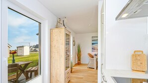 Una cocina con un armario de madera, una mesa de comedor con sillas y vista a un jardín césped a través de un ventanal grande.