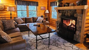 A cozy log cabin interior with a stone fireplace, wooden walls, a leather sofa, and a large clock.