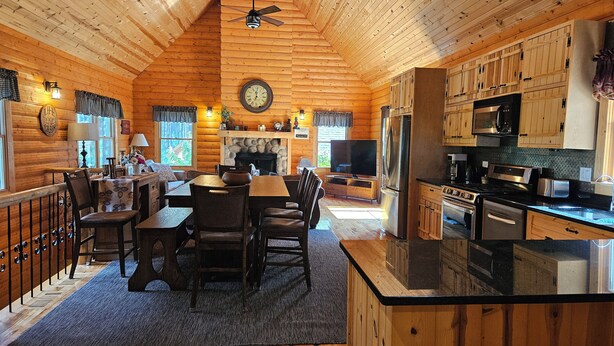 A log cabin interior with a dining area, kitchen, and fireplace.