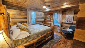 A log cabin bedroom with a bed, two windows, a desk, and a chair.