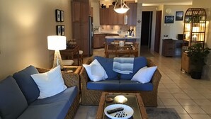 A living room with a sofa, a coffee table with remote controls, and a dining area with a table and chairs.
