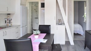 Una cocina compacta con armarios blancos, una mesa de comedor con sillas, una pequeña planta en maceta y una zona de ducha visible a través de una puerta abierta.