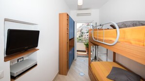 Une petite chambre comprenant un lit superposé, une télévision et un coin cuisine.