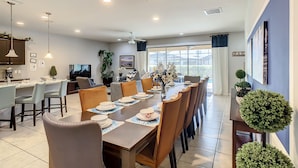 A modern dining area with a long table set for six, surrounded by chairs. - Lazy river pool and more! 9br/6ba pool villa from 300/nt,Close to Disney (Kissimmee)
