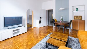 A modern living room with a flat-screen TV, wooden flooring, a dining area with a table and chairs, and a sofa.