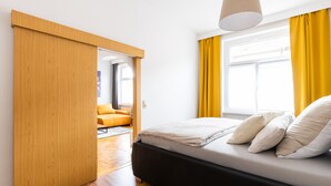 A modern bedroom with a bed, a wooden wardrobe, and a view of an adjacent room.