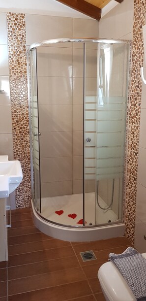 A corner shower with a glass door, a white sink, and a patterned wall. - Elena's Seaside Holiday House (Corfu)