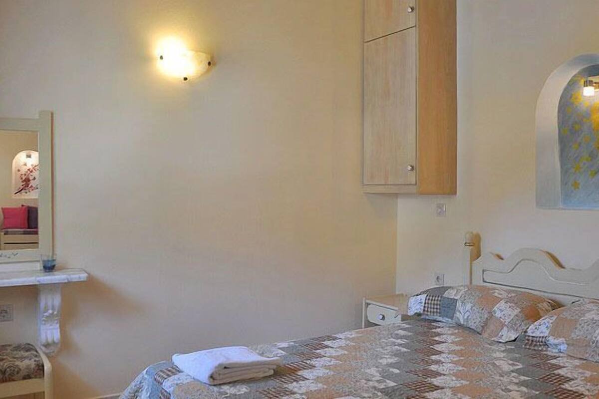 A bedroom with a bed, a nightstand, a mirror, a wall-mounted cabinet, and a wall decoration.