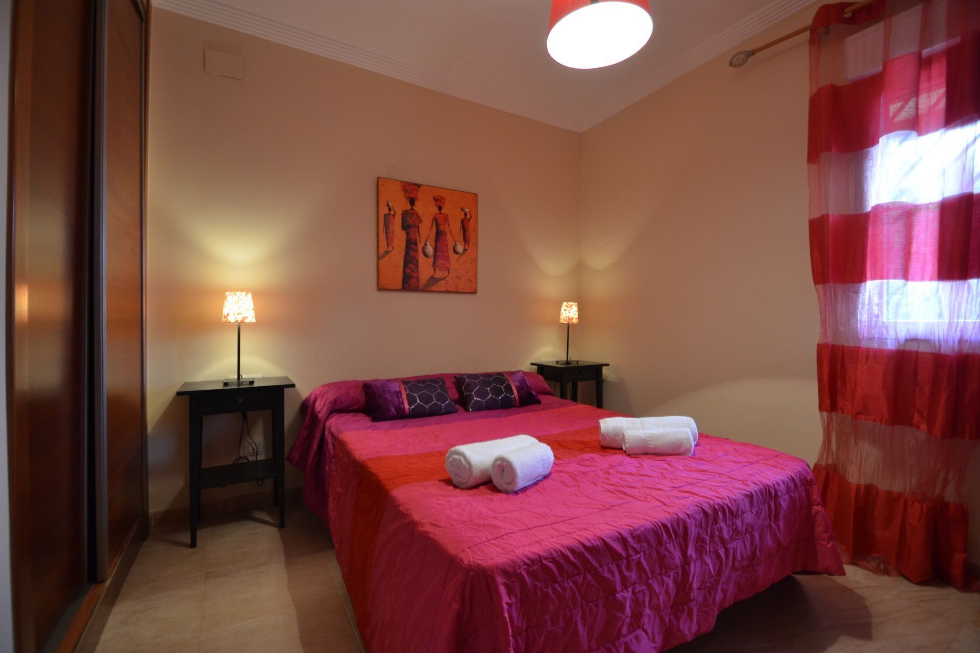 Une chambre d’hôtel avec un grand lit, deux tables de chevet, un tableau au mur et un rideau rouge.