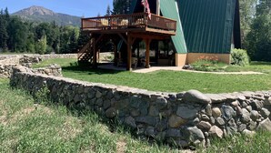 Een lodge met een houten terras en stenen muren, gelegen in een bergachtig gebied met een heldere lucht.