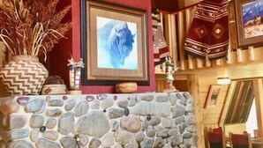 Een stenen openhaard met daarboven een lijstwerk met een foto, een groot gewei aan de muur en een rustiek houten plafond.