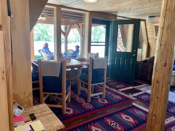 A wooden interior with a dining area, a green door, and patterned rugs.