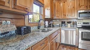 A kitchen with wooden cabinets, granite countertops, stainless steel appliances, and a sign that reads "Welcome to our Cabin". - Panoramic View - Suite 2: Brand New Hot Tub - Room w/ French Doors to Porch (sevierville)