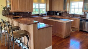 Una cocina moderna con armarios de madera, una isla central, taburetes de bar y un lavavajillas de acero inoxidable.