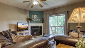 A living room with a fireplace, leather sofas, a television, and a ceiling fan. - On the River w/Balcony Views • 3 King beds • Virtual Checkin (Pigeon Forge)