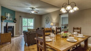 A dining room with a wooden table set for four, a fireplace, and a ceiling fan. - On the River w/Balcony Views • 3 King beds • Virtual Checkin (Pigeon Forge)