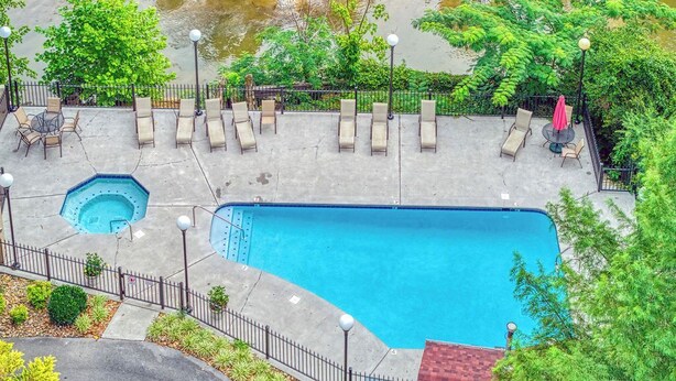 A rooftop pool area with lounge chairs and a small hot tub, surrounded by greenery and a view of a river. - On the River w/Balcony Views • 3 King beds • Virtual Checkin (Pigeon Forge)