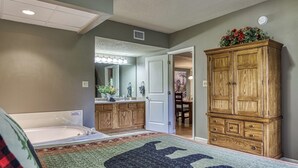 A bedroom with a large bed, a wooden wardrobe, a bathroom with a bathtub, and a mirror. - On the River w/Balcony Views • 3 King beds • Virtual Checkin (Pigeon Forge)