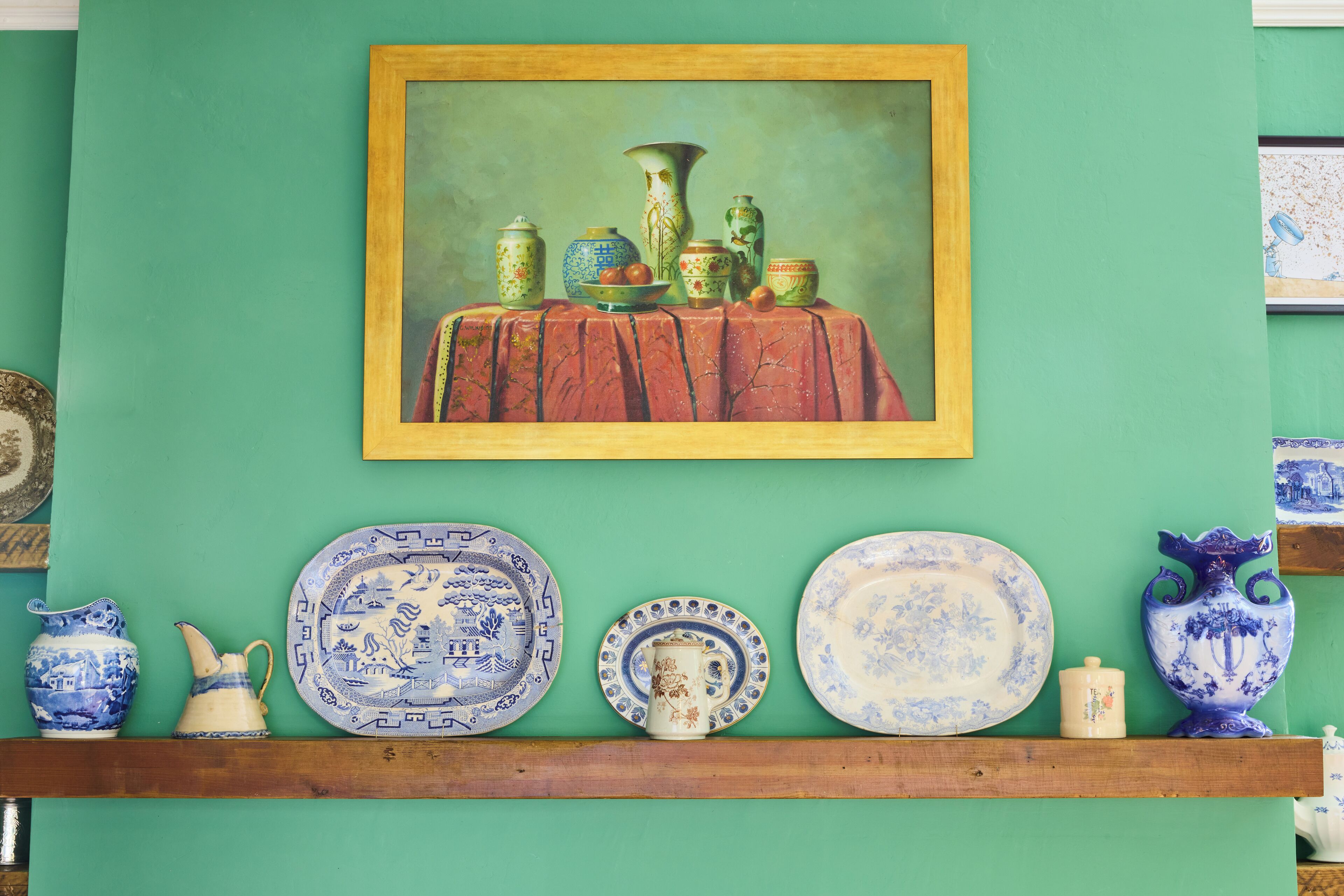 Una colección de artículos de cerámica azul y blanca exhibida en un estante frente a una pared verde.