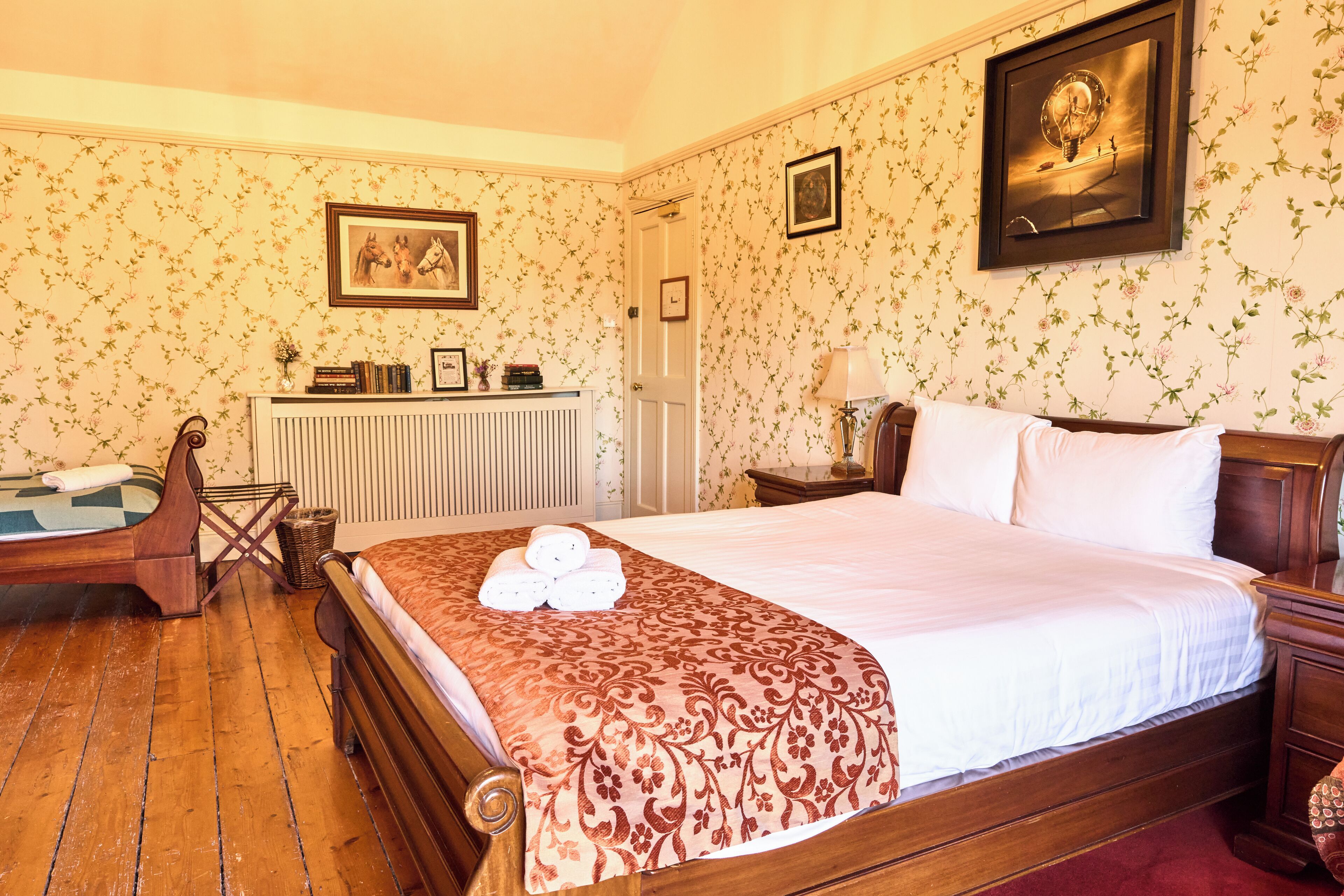 Una habitación de hotel con una cama de madera, un escritorio, un radiador y papel tapiz con motivos florales.