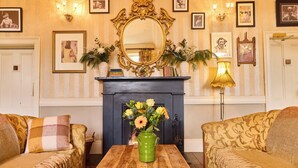 Une pièce avec deux canapés, une table en bois, un vase vert rempli de fleurs, une cheminée et des tableaux encadrés accrochés au mur.