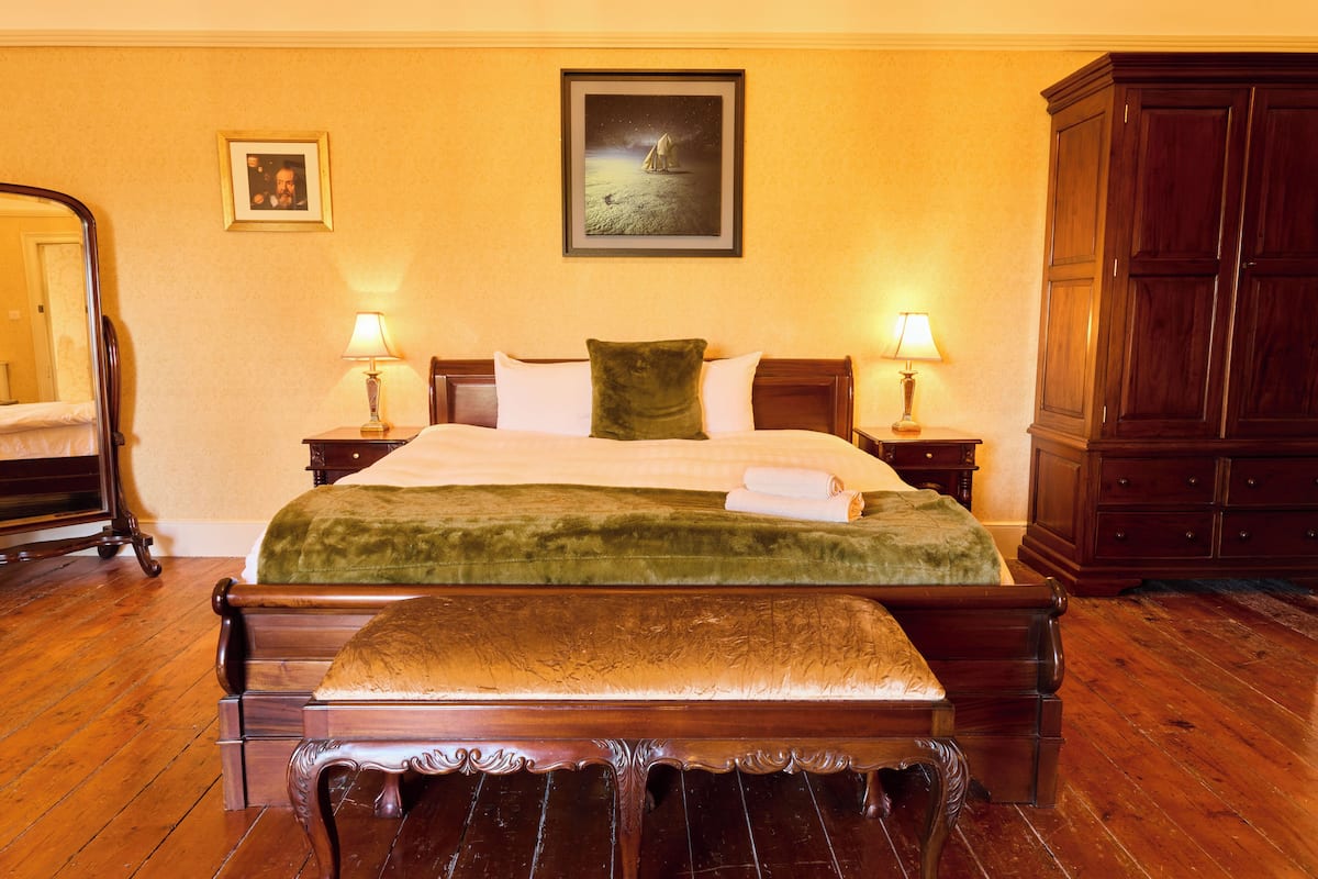Un dormitorio tradicional con una cama de madera, dos lámparas de noche, una manta verde, un banco de madera y un armario grande.
