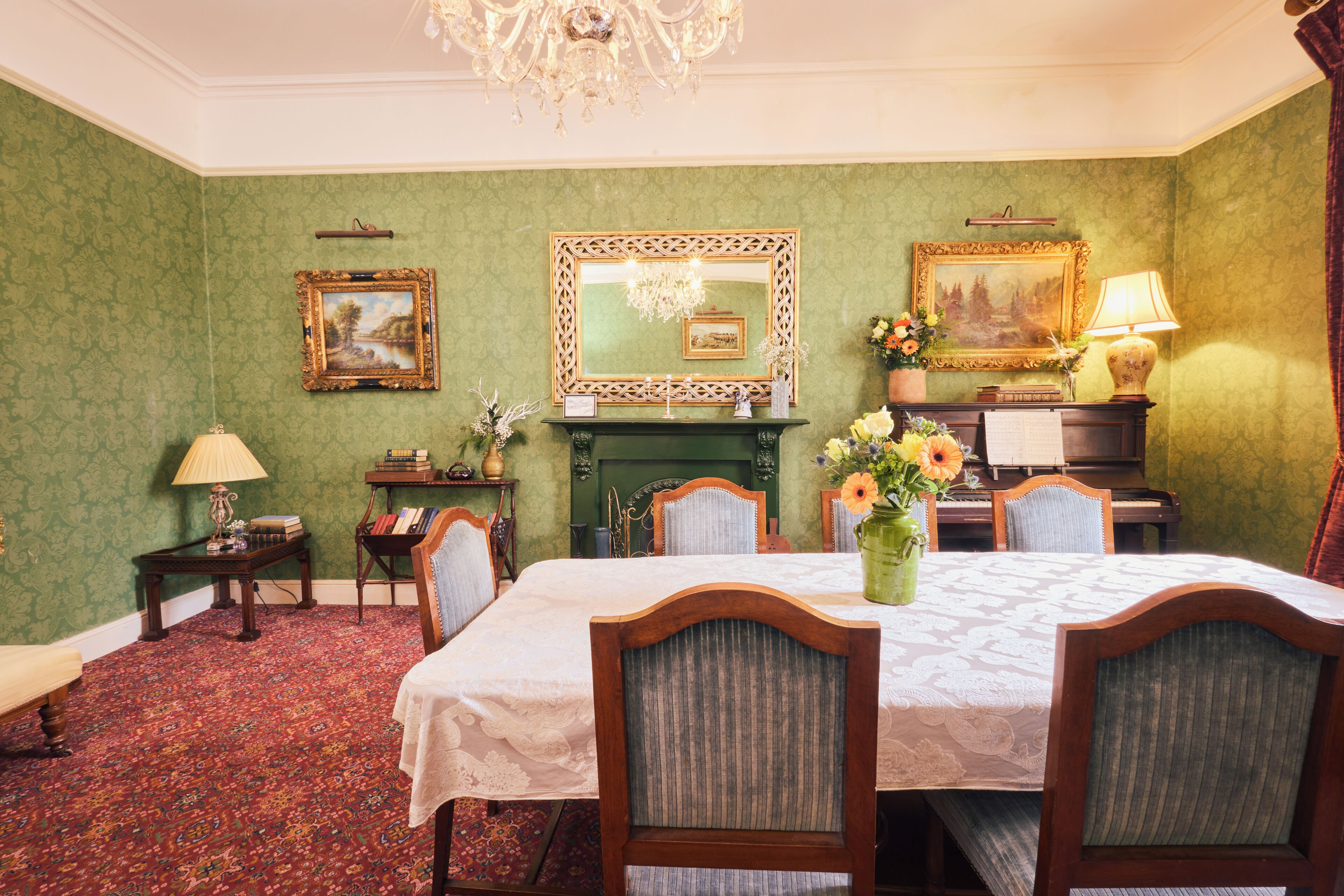 A dining room with a table set for four, surrounded by chairs, a fireplace, and framed artwork on the walls.