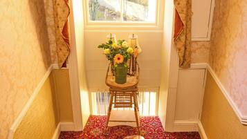 A carpeted staircase with a wooden handrail, a small table with flowers, and a window with curtains.