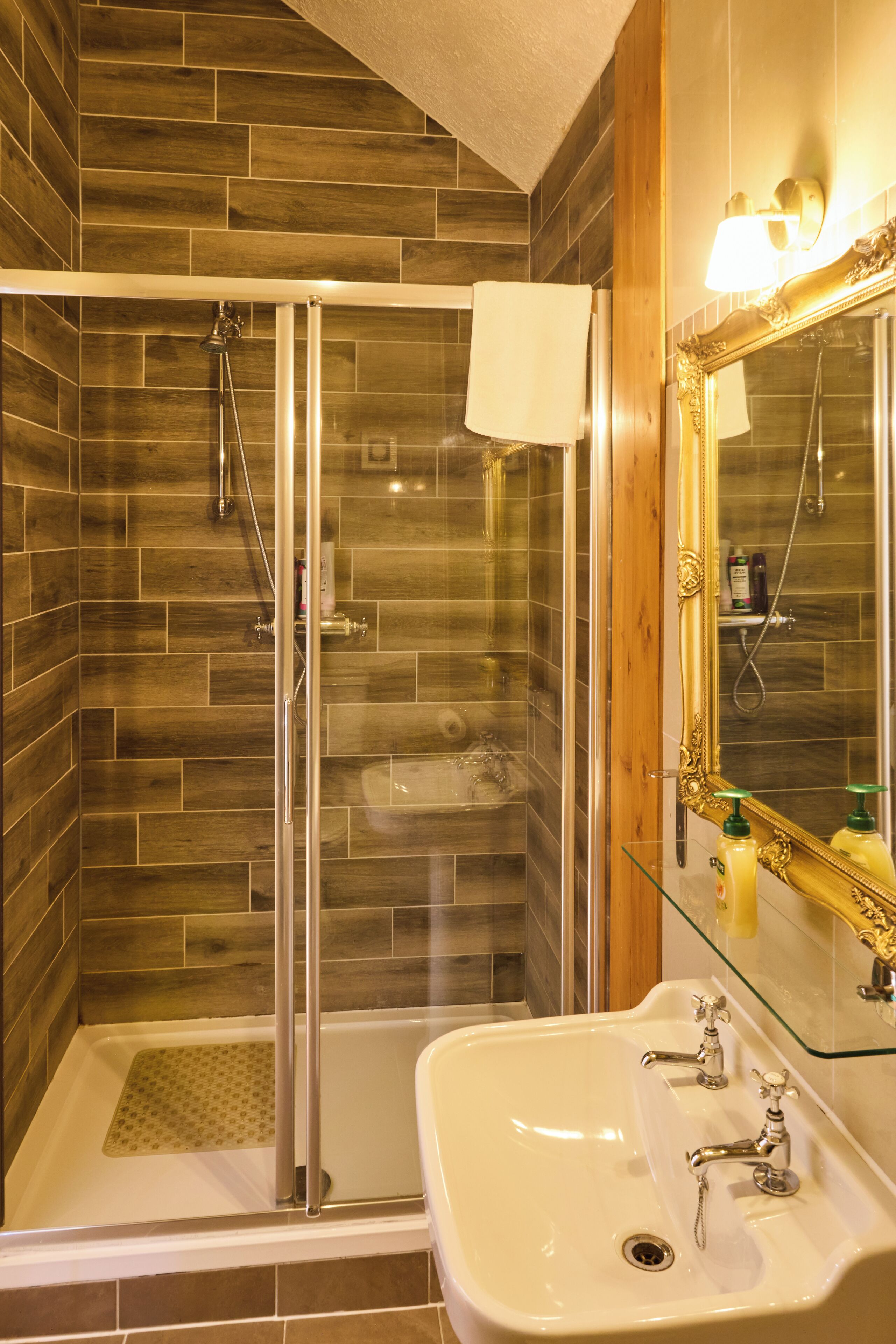 A bathroom with a glass-enclosed shower, a white sink, and a large mirror with a gold frame.