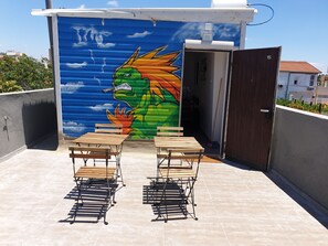 A small outdoor seating area with two wooden tables and metal chairs, a mural of a dragon on the wall, and a door marked with the number 15. - AirTLV Ben Hasher Apartments (Tel Aviv)