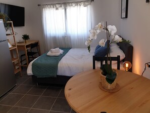 A neatly arranged bedroom with a bed, a bedside table with a lamp, a chair, a desk, and a small potted plant. - AirTLV Ben Hasher Apartments (Tel Aviv)