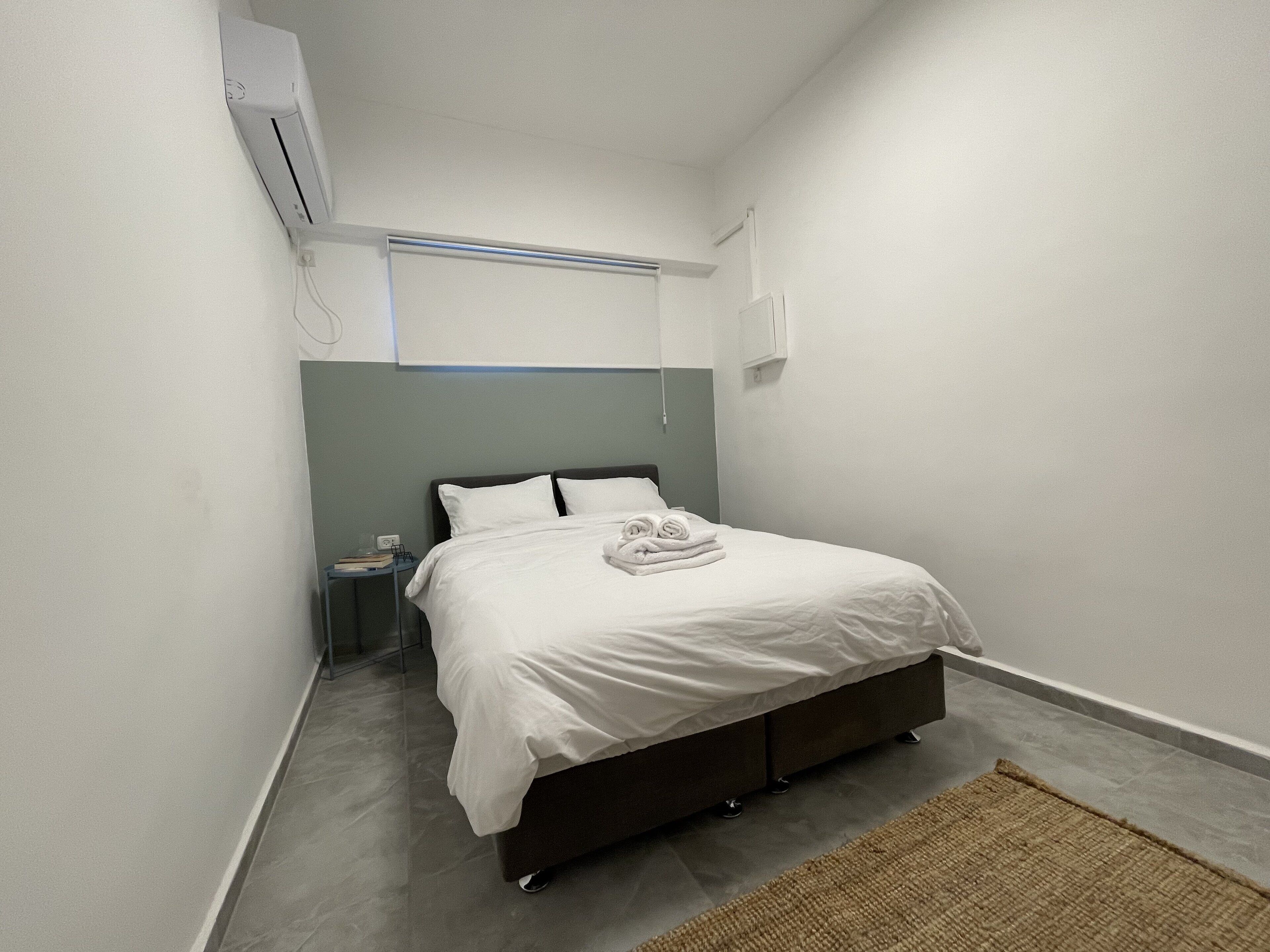 Una camera da letto piccola e moderna con un letto singolo, un comodino e un condizionatore d'aria a parete.