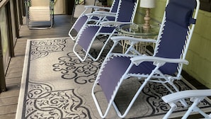 A covered porch with four lounge chairs, a glass table, and a ceiling fan. - Stilt home close to MacRaes, city dock, Wild Life Park. (Homosassa)