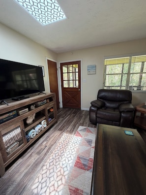 Un salon comprenant un téléviseur, un meuble de rangement en bois, un canapé en cuir et un tapis à motifs.