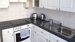 Una cucina con mobili bianchi, un piano di lavoro nero, un lavandino in acciaio inossidabile, un bollitore e un forno.