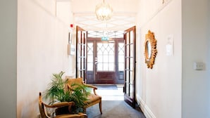 A hallway with a wooden bench, potted plants, a chandelier, and a door with glass panels. - Luxury Serviced Apartment with Daily Room Clean, Staffed Reception, King Size Be (London)