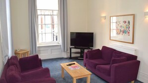 A living room with two purple sofas, a wooden coffee table, a TV, and a window with curtains. - Luxury Serviced Apartment with Daily Room Clean, Staffed Reception, King Size Be (London)