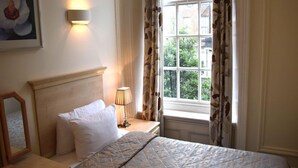 Ein Hotelzimmer mit Bett, Nachttischlampe, einem Fenster mit Vorhängen und einer Wandleuchte.