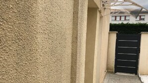 Ein schmaler, überdachter Außenkorridor mit einer strukturierten Wand an einer Seite und einem schwarzen Tor am Ende.