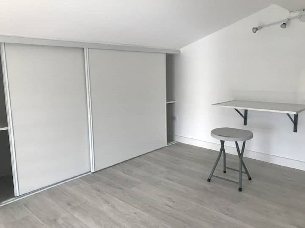 Une pièce avec un placard à porte coulissante, un petit tabouret et une étagère blanche.