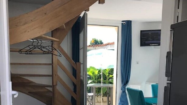 Ein gemütlicher Wohnraum mit einer Couch, einem kleinen Tisch, einer Treppe und einem Balkon mit Blick auf Grünflächen.