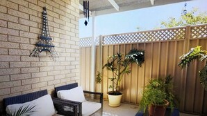 A covered patio area with a brick wall, a decorative Eiffel Tower, wicker furniture, potted plants, and a wooden fence. - Modern Townhouse close to CBD (Bendigo)