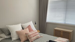 A neatly made bed with striped bedding and multiple pillows, a bedside table with a lamp, and a window with blinds. - Modern Townhouse close to CBD (Bendigo)
