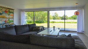 Uma sala de estar moderna com um sofá cinzento grande, uma mesa de centro branca e vista para um campo gramado através de grandes janelas.